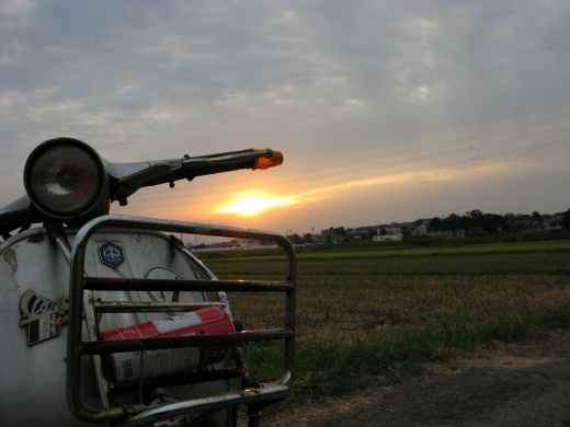 夕暮れの田んぼ道でたたずむベスパの後ろ姿