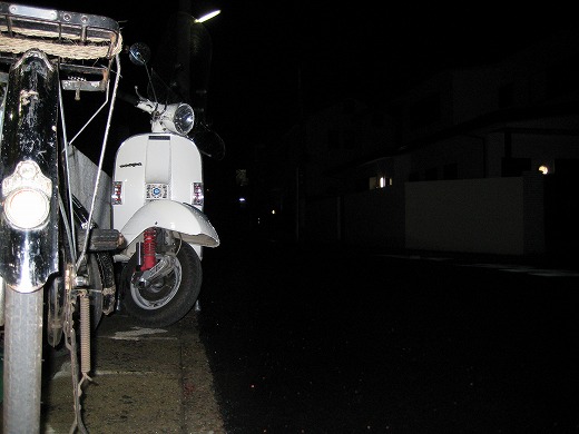 雨上がりの夜道に停められた白いベスパの写真