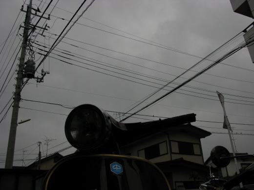 ベスパのヘッドライト越しに見上げたどんより曇った空と電線の写真