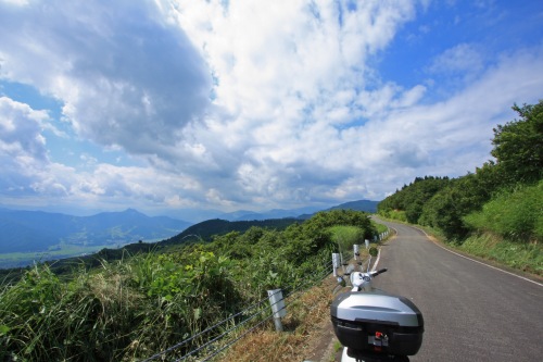 青空の下、山道に停まるシルバーのベスパと広がる絶景