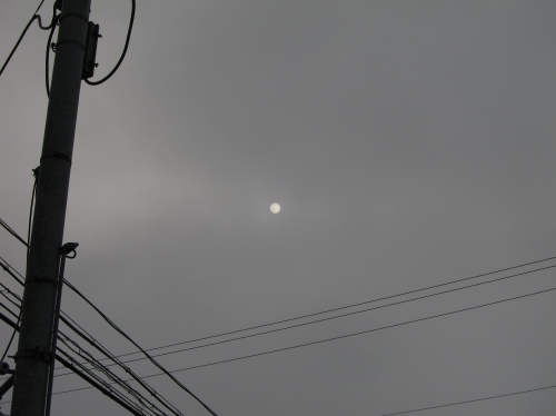 曇り空にうっすらと浮かぶ太陽と電柱、電線