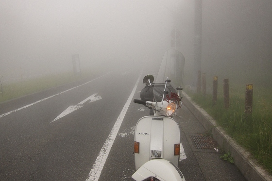 濃霧の中で停止した白いベスパと見通しの悪い道路。