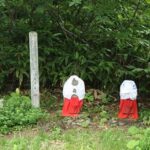 森の中に佇む三体の地蔵像。白と赤の衣をまとい、静かにたたずんでいる様子が印象的