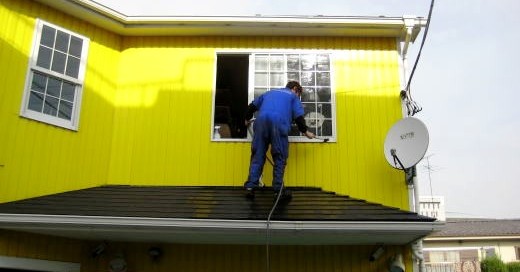 黄色い外壁の２階建て建物で窓を掃除するＫＢ社長の姿