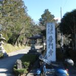 　道路沿いの木々に囲まれた鳥居と、その手前に停められた青いベスパ