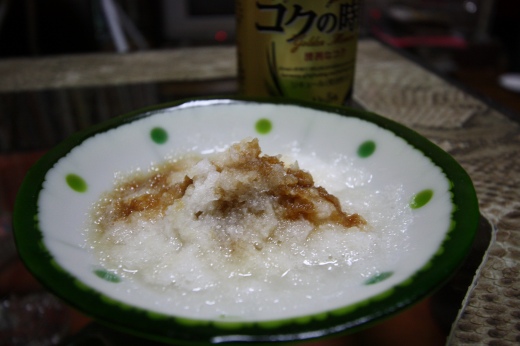 おろしポン酢がたっぷりかかった大根おろしの一皿。奥には缶ビールがぼんやり写る。