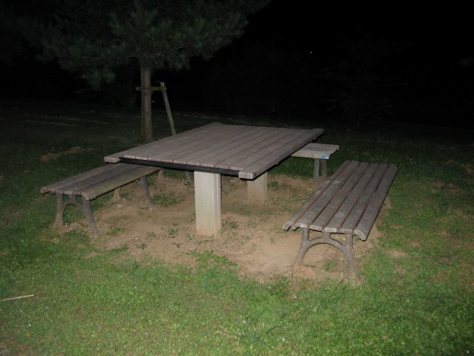 夜の公園にある木製のベンチとテーブルセット。草地の中に静かに置かれている。