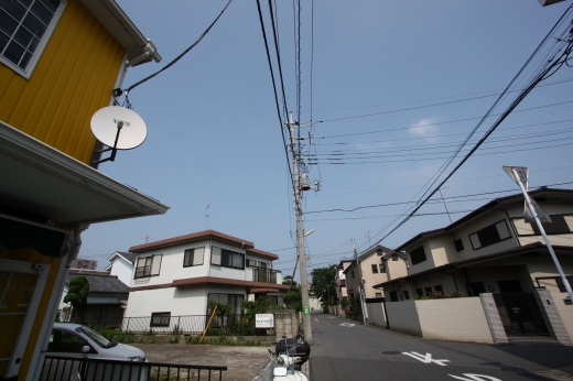 屋外の住宅街の風景。快晴の青空と電線、周囲の住宅が写っている。