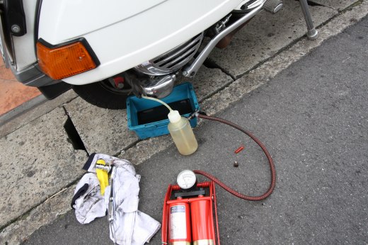 手のひらの上に載せたクランクシャフトのオイルシール。背景に白い車体が写っている。