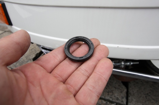 ベスパのフライホイール下でオイルシール交換中の様子。オイルや工具が舗装路上に並んでいる。