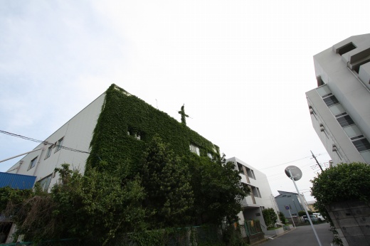 ツタに覆われた建物の屋上に立つアンテナのような十字架