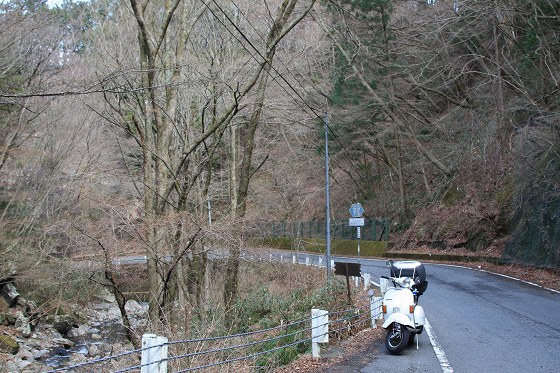 カーブを走り抜けた後に休憩する白いベスパと山道