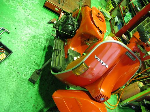整備中のオレンジ色のベスパと作業場の風景