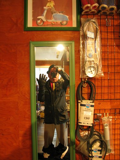 鏡に写った冬支度の人物とVespaパーツが並ぶ店内