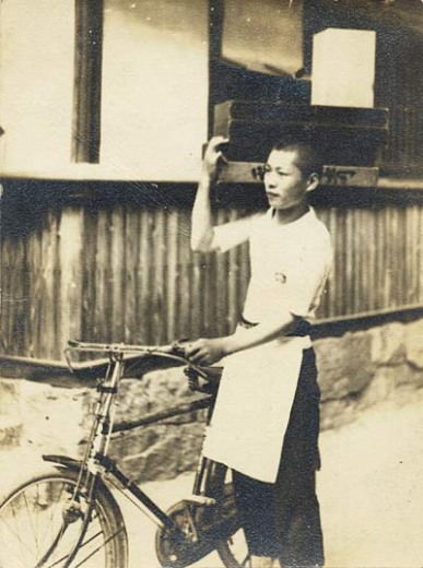 自転車で片手に弁当箱を持つ配達中の女性の姿