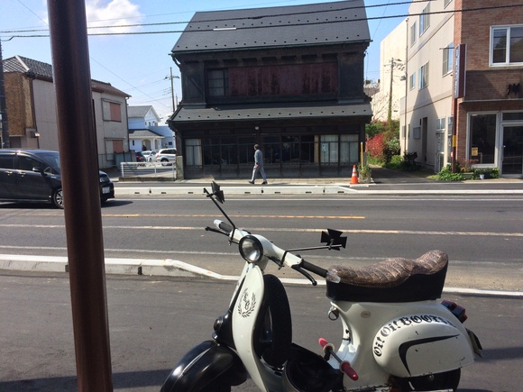 古い商家風の建物と、その前に停められた白いベスパのある風景