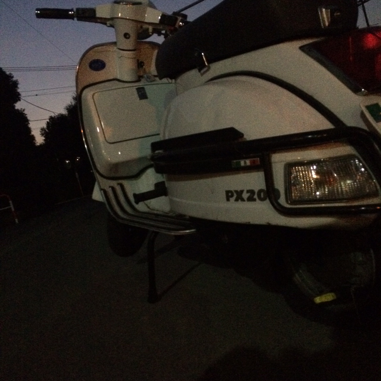 夕暮れ時に路上でスタンドを立てたまま停車している白いベスパPX200