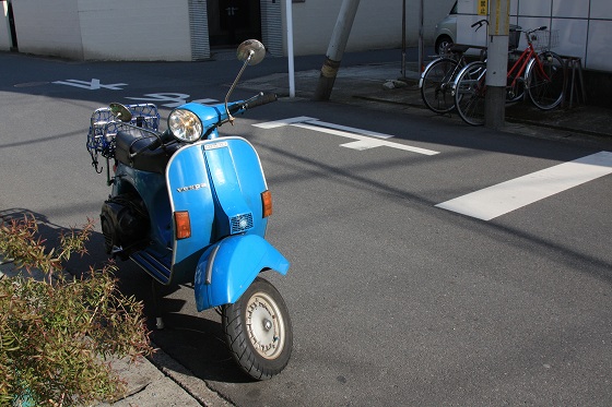 晴天の下、路肩に停められたブルーのベスパ。