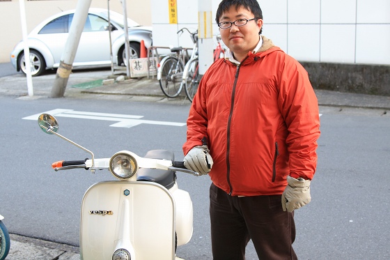ベスパの横に立つ赤いジャケット姿の男性の納車記念写真。
