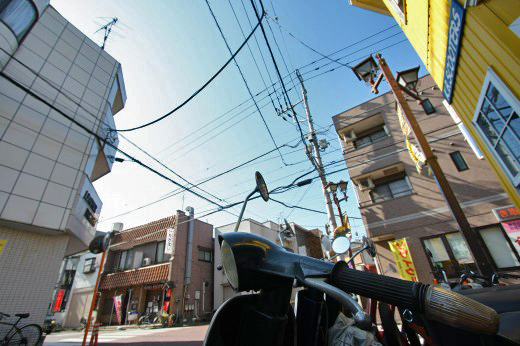 外に並んだ赤と白の椅子と木製スツール、日差しが差し込む店先の風景