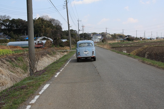 道路をゆっくり走るクラシックなDATSUN211とベスパの後ろ姿。