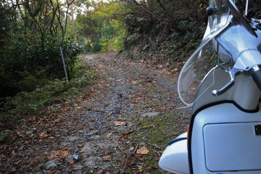 未舗装路の先に構えるベスパの斜め後方