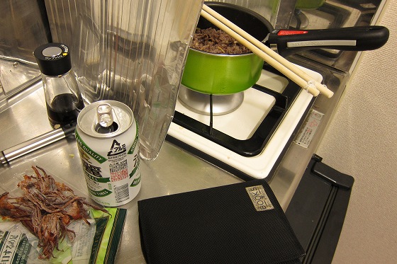 文庫本とビール片手に煮込み中の鍋をかき混ぜている様子。