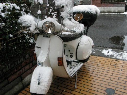 雪をかぶった白いベスパが駐車場に止まっている朝の様子