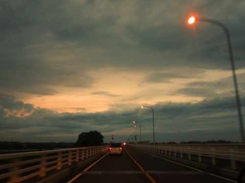 夕暮れの橋の上を走る車と街灯の光が印象的な風景