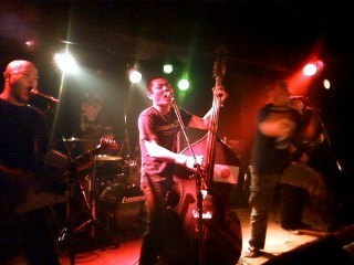 The VOi!CESのライブ演奏中のステージ風景、ウッドベースを弾くメンバーの姿。