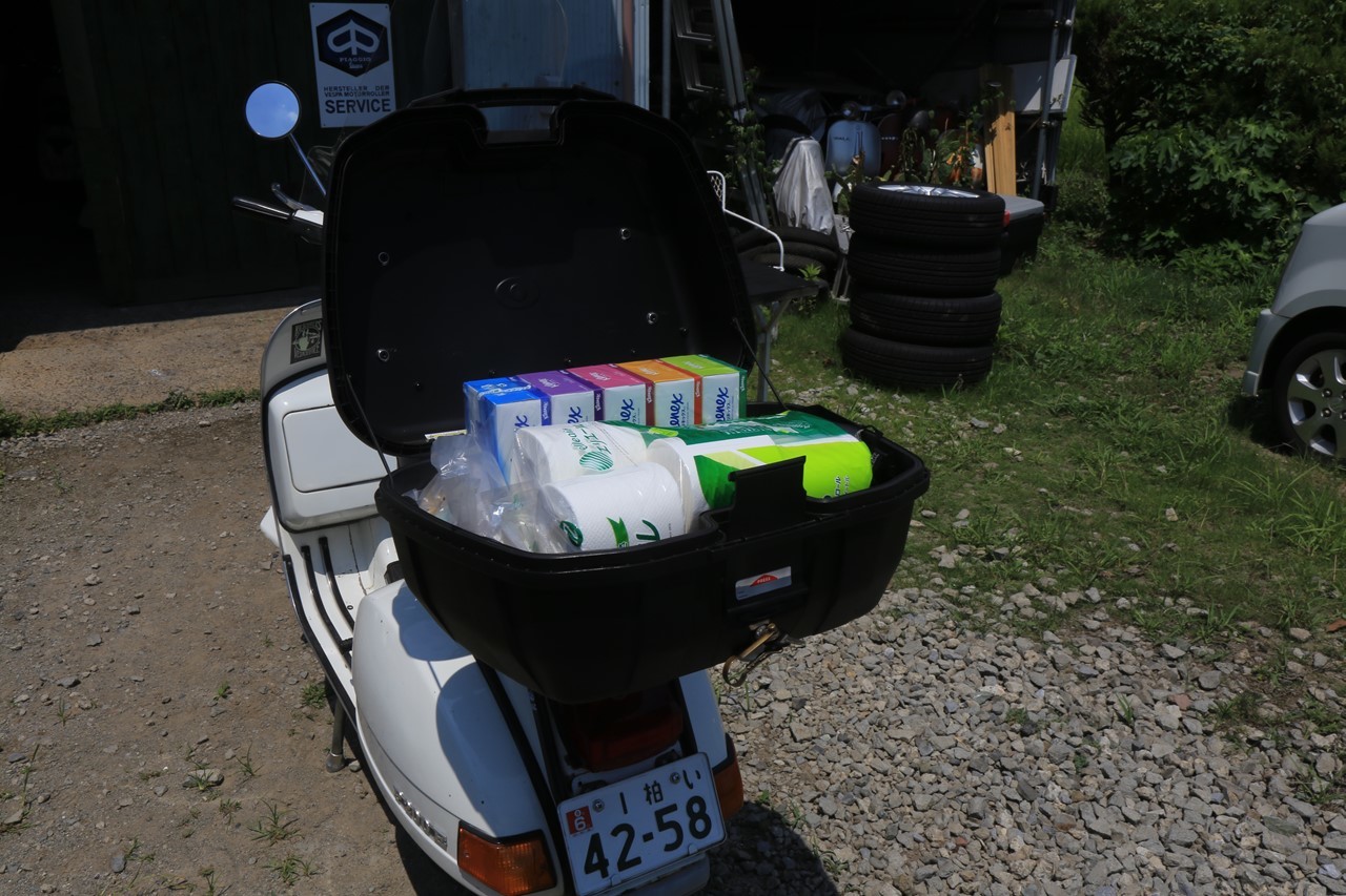 真夏の暑さの中ベスパで買い物に出かける場面