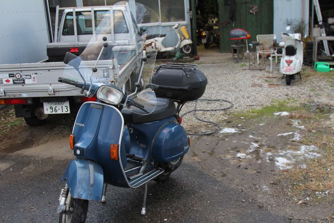 別の青いベスパP125Xが、屋外で洗車後のように停められている様子。
